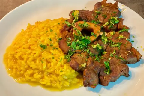 Un piatto di ossobuco alla milanese con risotto giallo, guarnito con prezzemolo fresco e scorza di limone.