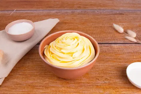 Una ciotola piena di soffice crema al burro, pronta per decorare torte. Accanto, ciotoline con zucchero e decorazioni naturali.