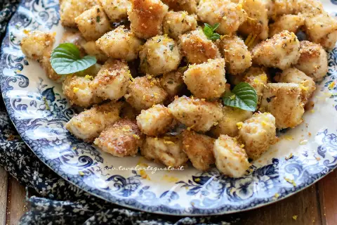 Bocconcini di pollo dorati e croccanti, guarniti con scorza di limone e foglioline di menta, su un piatto decorato.