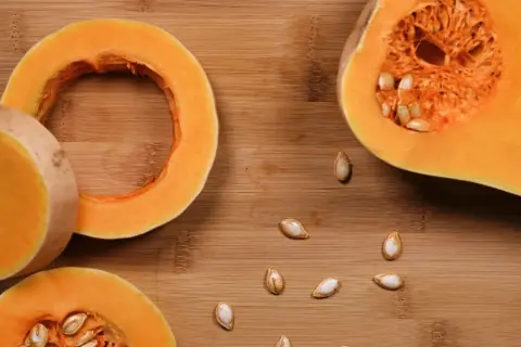 Fette di zucca pronte per essere cotte in padella, con semi sparsi sul tagliere di legno.