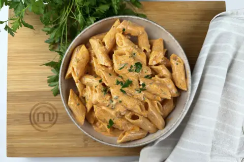 Penne alla vodka cremose e invitanti, guarnite con prezzemolo fresco, su un tagliere di legno con il logo di MasterChef.