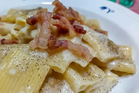 Un piatto di pasta alla gricia fumante, con guanciale croccante e abbondante pepe nero.