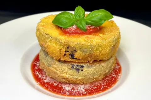 Due cordon bleu di melanzane impilati, dorati e croccanti, su salsa di pomodoro e basilico fresco.