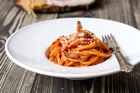 Un piatto di spaghetti alla amatriciana, con guanciale croccante e una salsa rossa saporita. La cipolla, ingrediente chiave della ricetta originale, dona un tocco in più.