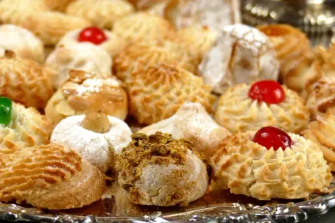Vassoio pieno di biscotti alle mandorle morbidi, alcuni decorati con ciliegie candite, mandorle e pistacchi.