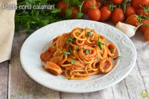 Un piatto di spaghetti con anelli di calamari e pomodoro, guarnito con prezzemolo fresco.