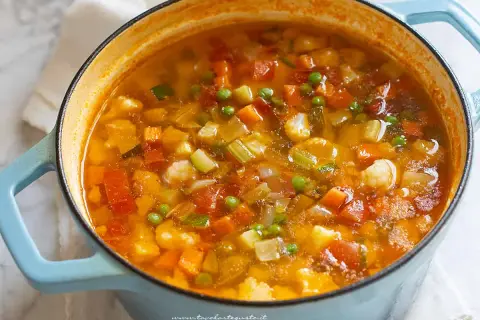 Un fumante minestrone di verdure in una pentola azzurra, ricco di carote, zucchine, piselli e cavolfiore.
