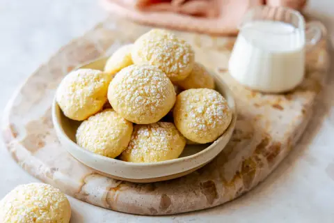 Una ciotola piena di biscotti da inzuppo spolverati di zucchero a velo, pronti per essere gustati con un bicchierino di latte.