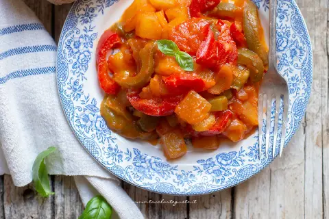 Un piatto di peperonata con patate, colorato e invitante, guarnito con basilico fresco.