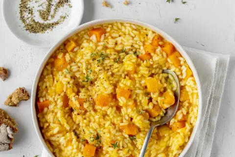 Un cremoso risotto con la zucca, guarnito con timo fresco e pepe nero macinato. Accanto, pane rustico e una ciotolina di pepe.