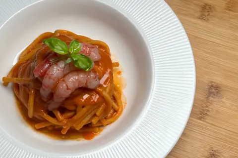 Spaghetti al sugo di pomodoro con gamberi freschi e basilico, un piatto che evoca il sapore intenso della bisque di gamberi.