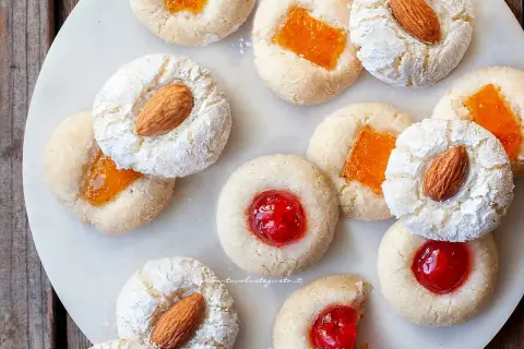 Biscotti alla pasta di mandorle con mandorle intere, marmellata d'arancia e ciliegie candite, spolverati di zucchero a velo.