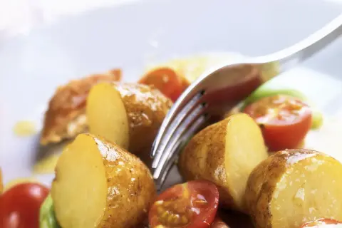 Patate novelle tagliate a metà, pomodorini e un tocco di verde compongono questa fresca insalata di patate estiva, pronta per essere gustata.