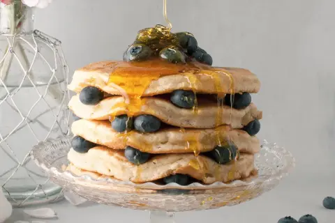 Pancake senza latte, una torre dorata con mirtilli freschi e sciroppo d'acero che cola. Delizioso e leggero, perfetto per ogni momento.