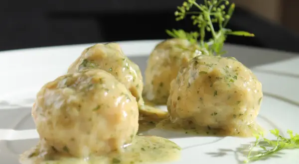 Quattro polpette in bianco su un piatto bianco, condite con una salsa cremosa e erbe aromatiche.
