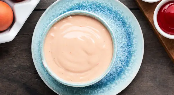 Una ciotola di salsa rosa cremosa, perfetta per la tua prossima ricetta. Accanto, uova e condimenti.
