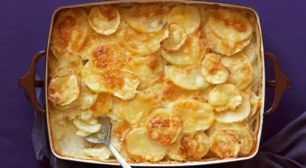 Parmigiana di patate dorata e cremosa, appena sfornata, con una fetta servita.