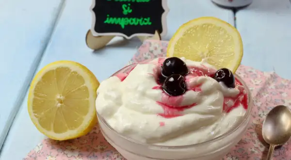 Deliziosa mousse al limone con ciliegie e una fetta di limone, servita in una ciotola su un tovagliolo fiorato.