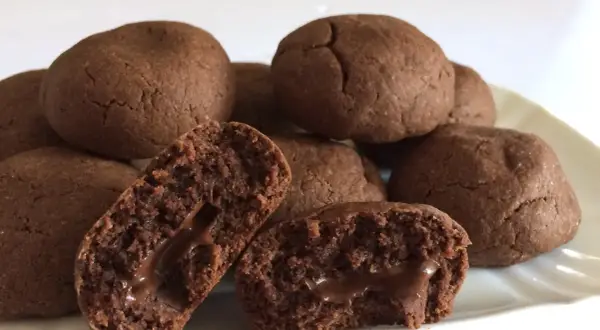 Biscotti al cioccolato morbidi con cuore filante. Alcuni sono interi, altri spezzati per mostrare il ripieno goloso.