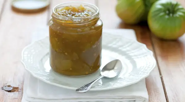 Un vasetto di marmellata di pomodori verdi, con pomodori verdi sullo sfondo.