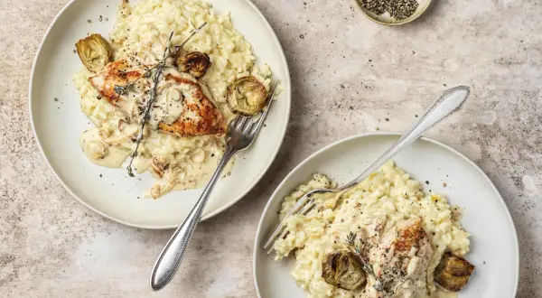 Due piatti di cremoso riso con pollo, guarniti con carciofi e rosmarino. Un piatto invitante e saporito.