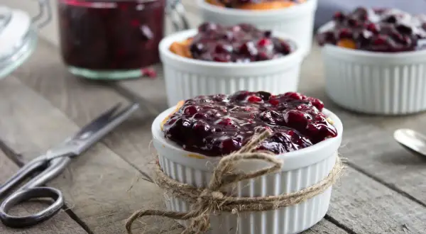 Deliziosa marmellata di amarene ricetta in ciotoline, pronta per essere gustata. Un vasetto pieno e forbici vintage completano la scena.