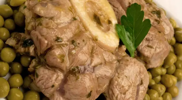 Ossobuco con piselli, un piatto succulento con carne tenera e piselli verdi brillanti, guarnito con una foglia di prezzemolo.