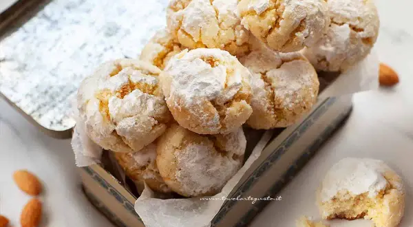 Biscotti con farina di mandorle, spolverati di zucchero a velo, in una scatola vintage. Alcune mandorle intere sono sparse intorno.