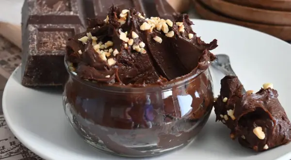 Un delizioso budino al cioccolato, cremoso e guarnito con nocciole tritate, accanto a una tavoletta di cioccolato fondente.