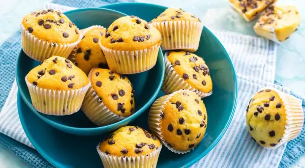 Muffin con gocce di cioccolato dorati e soffici, serviti in una ciotola blu.