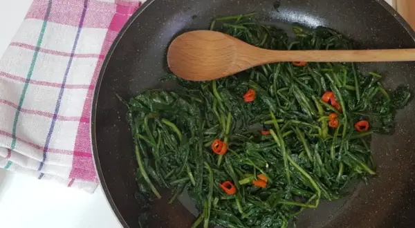 Cicoria in padella, un contorno saporito con peperoncino e un cucchiaio di legno pronto a mescolare.