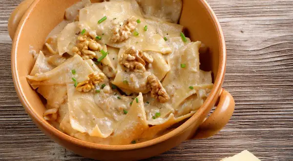 Pasta con cremoso pesto di noci, guarnita con noci intere e erba cipollina, servita in una ciotola di terracotta.