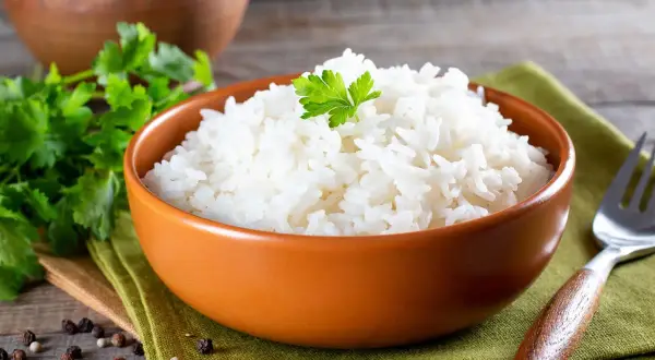 Un invitante piatto di riso in bianco, guarnito con prezzemolo fresco, su un tovagliolo verde. Accanto, grani di pepe e una forchetta.