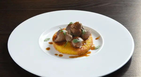 Delizioso riso al salto con bocconcini di carne e salsa bruna, guarnito con erbe fresche su un piatto bianco.