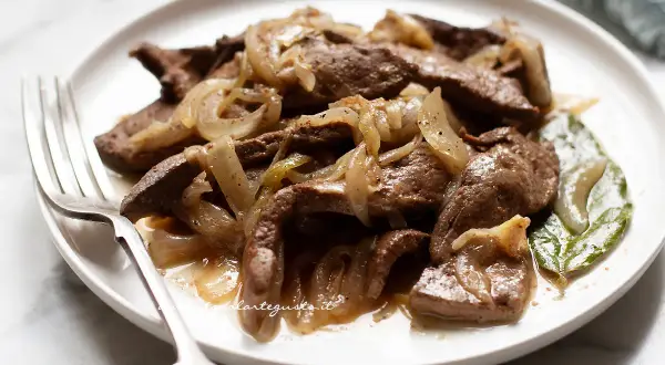 Piatto di fegato alla veneziana con cipolle caramellate, servito su un piatto bianco con una forchetta.