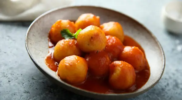 Gnocchi di pane in salsa rossa, un piatto rustico e saporito, servito in una ciotola di ceramica grezza.