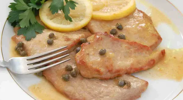 Scaloppine al limone succulente, guarnite con capperi, prezzemolo fresco e fette di limone. Una forchetta attende il primo assaggio.