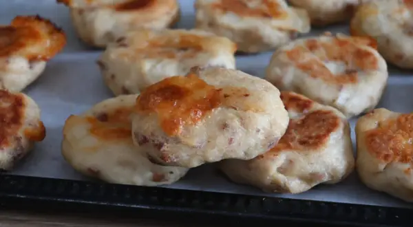 Polpette di pollo dorate e gustose, appena sfornate, con formaggio fuso e pezzetti di carne visibili.
