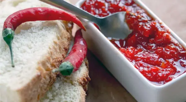 Fette di pane con peperoncini rossi e una ciotolina di marmellata di peperoncino, pronta per essere gustata.