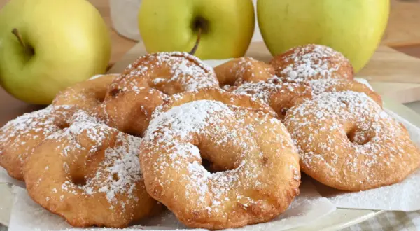Frittelle di mele dorate e zuccherate, pronte per essere gustate. Tre mele verdi sullo sfondo.