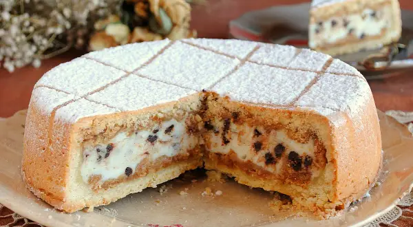 Una fetta di cassata al forno, con ripieno cremoso e gocce di cioccolato, cosparsa di zucchero a velo.