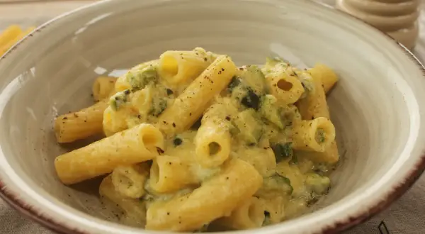 Piatto di rigatoni cremosi con carbonara di zucchine, guarniti con pepe nero macinato fresco.