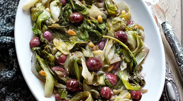 Scarola in padella con olive nere e pinoli, un contorno saporito e colorato, pronto per essere gustato.