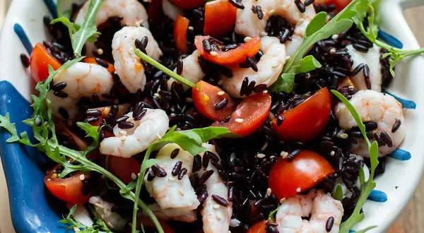 Insalata colorata con riso venere, gamberetti succosi, pomodorini freschi e rucola croccante. Un piatto leggero e gustoso.