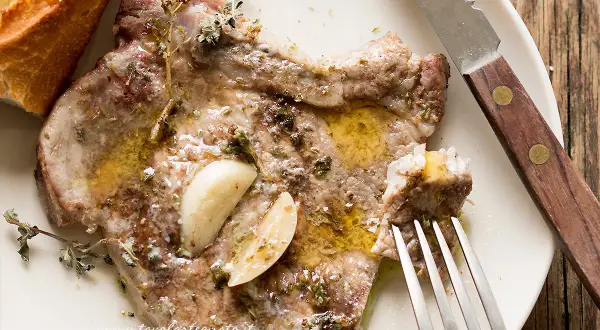 Succulenta braciola di maiale condita con aglio e erbe aromatiche, servita con pane croccante.