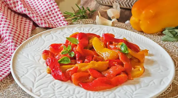 Peperoni rossi e gialli arrostiti in friggitrice ad aria, guarniti con basilico fresco, su un piatto bianco decorato.