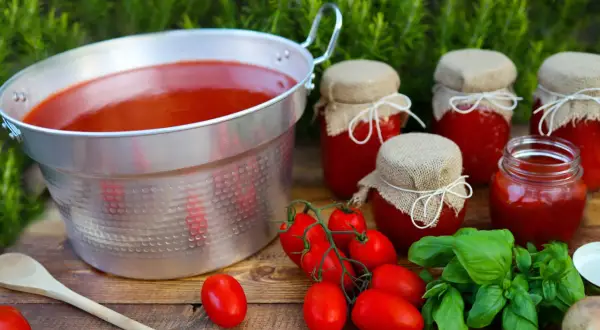 Un grande pentolone di passata di pomodoro, vasetti fatti in casa e pomodori freschi, pronti per la conservazione.