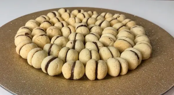 Baci di dama ricetta: biscotti friabili con ripieno di cioccolato, disposti a cerchio su un piatto dorato.