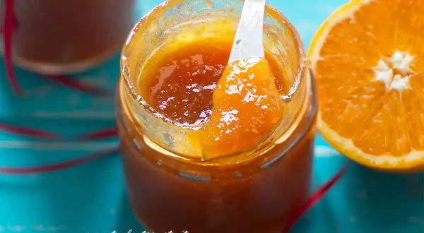 Un vasetto di marmellata di arance fatto in casa, con una fetta d'arancia accanto. La marmellata è lucida e invitante, pronta per essere gustata.