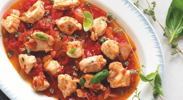 Piatto di coniglio alla cacciatora con pezzi di carne tenera in salsa di pomodoro e peperoni, guarnito con basilico fresco e erbe aromatiche.